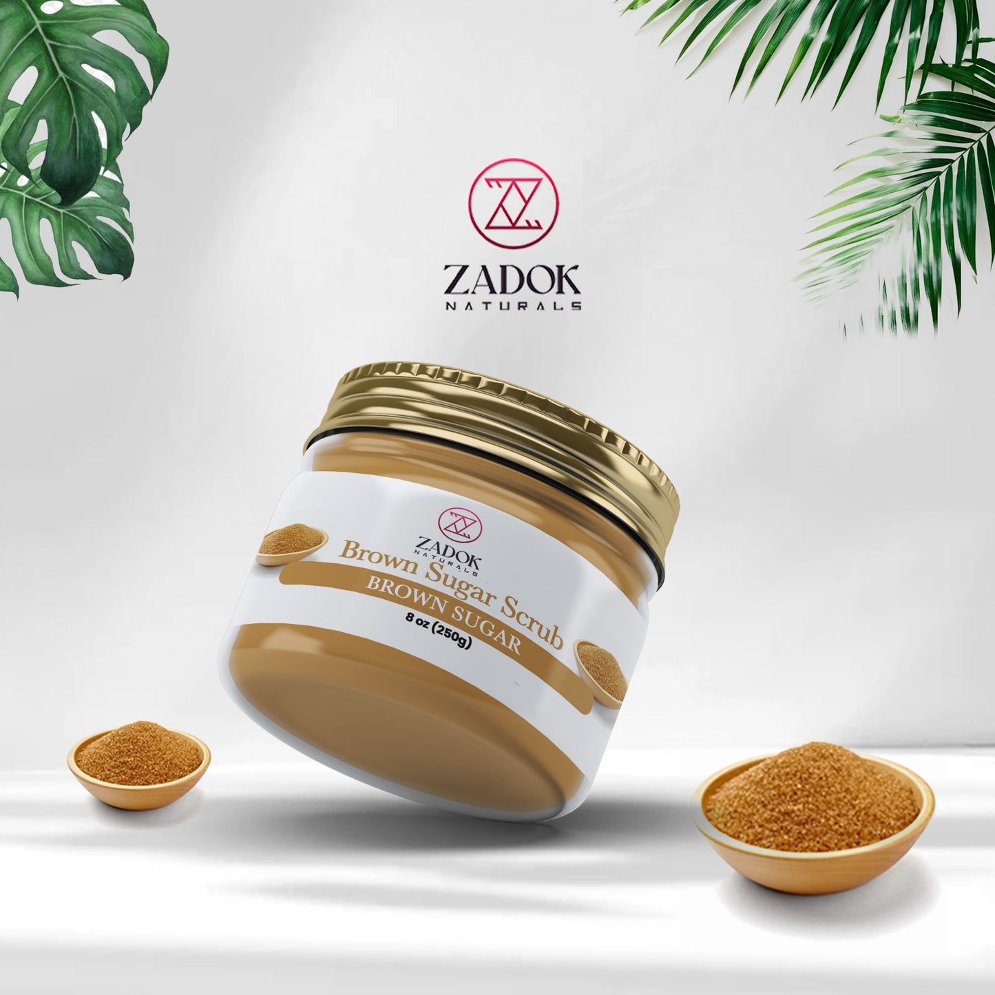 A jar of Zadok's Natural Brown Sugar Scrub with a white label, brown sugar crystals in front, and a green leafy background.
