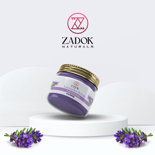 A jar of Zadok Naturals Lavender Scrub with a purple label, set against a white background with lavender flowers to the side.
